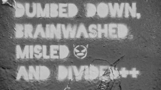 Black and white photograph of a graffiti reading "Dumbed down, brainwashed , misled and divided"
