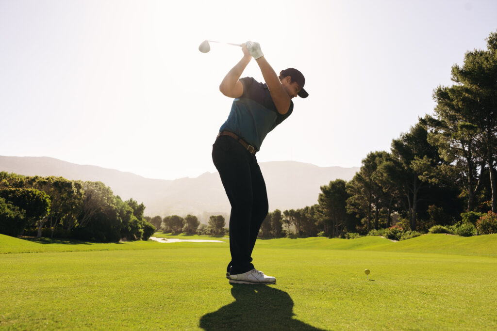 summer legal events illinois A man golfer skillfully swings his club during a fairway shot, with a golf ball in sight, surrounded by vibrant greenery under a clear sunny sky.