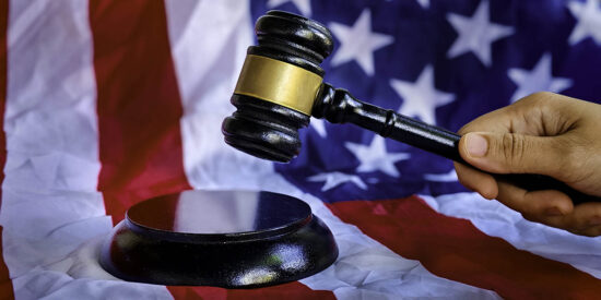 A hand holding gavel with background of usa flag.